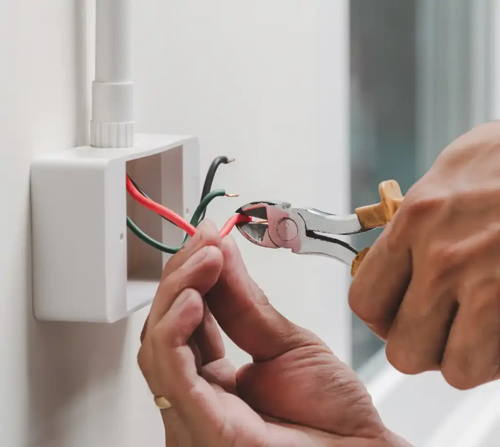 Elektricien snijdt elektrische draden binnen een wanddoos tijdens installatiewerk.