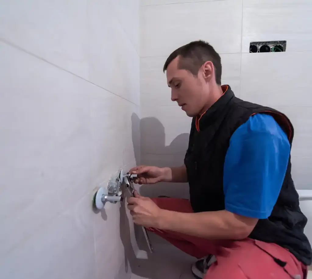 Loodgieter installeert een wateraansluiting voor de badkamer op een betegelde muur tijdens residentieel loodgieterswerk.